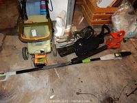 Photo showing Neuton electric lawn mower in green with battery charger, Black & Decker leaf blower, hedge trimmer, and Chicago pole saw on floor.