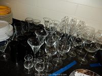 Over 40 assorted glassware items arranged on a black surface, including stemmed glasses, wine glasses, and cocktail glasses.