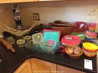 Overall kitchen counter setup showing Pyrex bowls, plastic cups, wooden bowls, food tents, and various glass storage items.