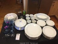 Full display of Noritake Ravel patterned white china with embossed floral and leaf design, matching serving platter, bowl, and covered casserole. Fostoria crystal stemware glasses visible to left side and Mikasa cups in back row.