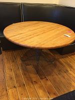 Front view of the round wooden top table with black cushioned booth seating in background and wood flooring