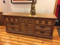 Front view of stripped wood French Provincial dresser with six drawers and central cabinet on wood floor