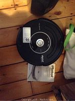 Top view of the black iRobot Roomba robot vacuum cleaner placed on wooden floor next to owner's manual.