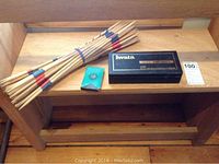 Photo showing wooden pickup sticks, green case of playing cards, and closed Iwata airbrush box.