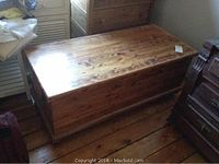 Closed wooden chest with visible wood grain sitting on wooden floor beside other furniture.