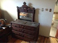 Photo of dark brown dresser with ornate wooden carved details and matching mirror behind it, showing overall lot items and condition.