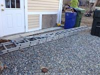 Full side view of a 28 foot Werner aluminum extension ladder resting on gravel outside a building.