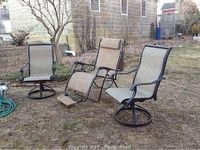Three outdoor chairs arranged on grass: a zero gravity recliner in the center with a headrest pillow, flanked by two swivel patio chairs with mesh seats and metal frames.