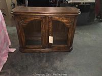 Front view of the wooden side cabinet showing glass doors, brass accents, and wood grain finish.
