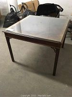 Full view of square glass top table with wooden frame and legs in a storage area.