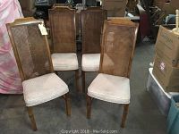 Four wooden dining chairs with caned backs and light upholstered seats arranged together.
