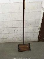 Full view of the wooden rug sweeper standing upright showing long wooden handle and rectangular wooden base with metal frame.