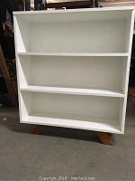 Front view of the white painted wooden bookcase showing three shelves.