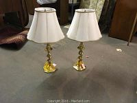 Pair of brass spiral column table lamps with white fabric scalloped lamp shades trimmed in gold, placed on floor.