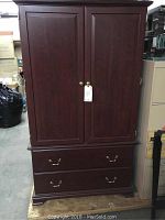 Front view of entire Sauder armoire showing two paneled doors on top and two drawers below with brass handles.