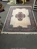 Full view of the ivory and rose polyester Shankar Aubusson rug showing floral medallion center and border with fringed edges.