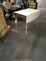 Full view of the table showing the overall shape, red and white paint, and drop leaf closed.