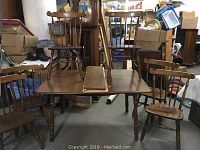 Overview of wooden kitchen table with two leaves on top and six chairs surrounding it in storage setting.
