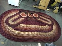 Large braided oval rug with three small oval rugs and three round seat mats arranged on a floor.