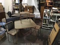 Vintage beige card table with 4 matching folding chairs in a room with various furniture and boxes.