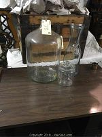 Three glass vessels on table: 6.5 gallon carboy, wine carafe, tobacco jar.