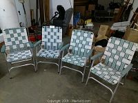 Four vintage folding lawn chairs with aluminum frames, green and white woven plastic seats and backs, and blue-green plastic armrests, set in a storage space with various items around.