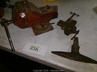 Photo showing two metal shop vises, one larger marked Shop King Wilton Chicago and one smaller marked Atol Mass, both with red paint and visible wear.