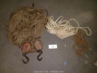 Full view of the vintage wood block and tackle with coiled hemp rope and rusty tow chain all lying on a concrete floor.