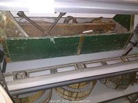 Wooden green painted tool carrier filled with various hand tools, including levels and other wooden-handled tools.