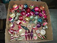 Box containing a collection of assorted colorful vintage mercury glass Christmas ornaments of different shapes.