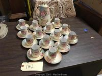 Overall view of the coffee set including 14 cups and saucers arranged around the coffee pot on a wooden table