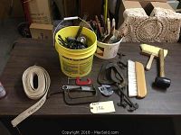 Photo of tools on a table including C-clamps, wrenches, paint brushes in buckets, black rubber mallet, and a hand brush