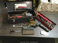 Open black metal toolbox with assorted hand tools including hammer, screwdrivers, files, scissors, and red metal tray with small parts.