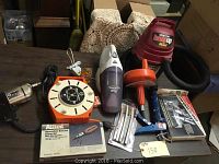 Various power tools and accessories including a handheld vacuum, ratchet driver set, extension cord reel, staple gun, Shop-Vac mini vacuum, wire wringer, drill bits, and replacement staples.