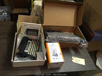 Overview of the lot showing the TTY phone in box, cordless answering system in its box, and the cable box tuner on the table.