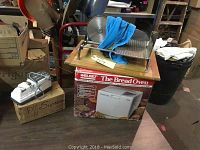 Photo shows a Welbilt Bread Oven bread machine in its original box, a metal bread slicer with a wooden base and blue cloth, and a white and gray electric knife sharpener arranged on a wooden surface.