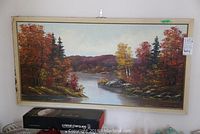 Full view of framed oil painting showing river landscape with autumn colored trees and distant hills.