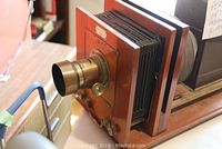 Front view showing brass focusing lens, wooden slide plate holder with multiple slots and foldable bellows