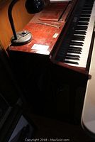 Side view of wood-finish piano with lamp on top