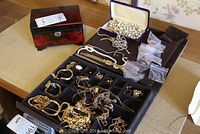 Full view of open black and red lacquered wooden jewellery box and multiple pieces of costume jewellery displayed inside and outside the box.