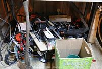 Tools and clamps under a table, including a long-handled metal tool leaning against the table and a cardboard box with heated pet dishes