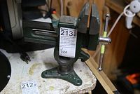 Front view of green metal bench vice on workbench showing base and jaws with wear.