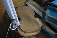 Woodworking bench with white adjustable-arm magnifying lamp and bench vise next to violin-shaped wood blank.