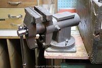 Close-up of metal bench vice mounted on wooden workbench, showing handle and jaws