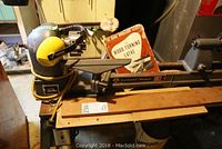 Full view of lathe mounted on metal stand with wood bed extensions and manual leaning at back