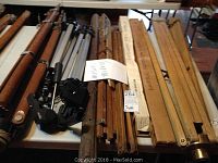 View of multiple tripods with wooden and metal components showing wear, scratches, and signs of use, arranged on a table.