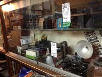 Glass shelf display with multiple vintage cameras and camera equipment including lenses, flash unit, and film boxes.