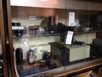 Glass display cabinet with Kodak Ensign camera, Supermatic 500 projector and other items inside.