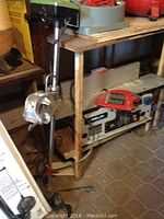 Full length view of Shakespeare Wondertroll Super 606 trolling motor leaning against a workbench with attached wiring and clamps on the floor.