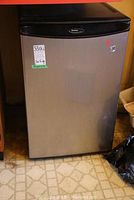 Front view of Danby bar fridge showing stainless steel door and black top trim with stickers.